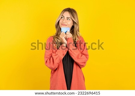 Photo of cheerful young beautiful blonde woman standing over yellow studio background hold debit card look empty space