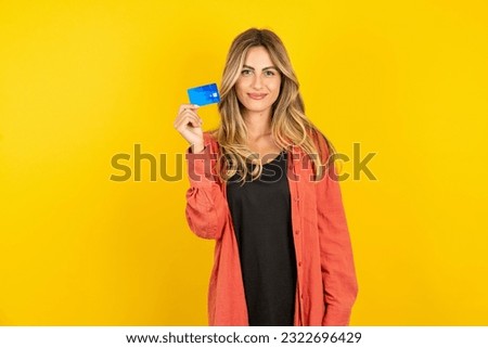 Photo of happy cheerful smiling positive young beautiful blonde woman standing over yellow studio background recommend credit card