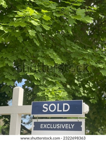 Sold sign on top of a real estate sign. Lush green foliage in the background.