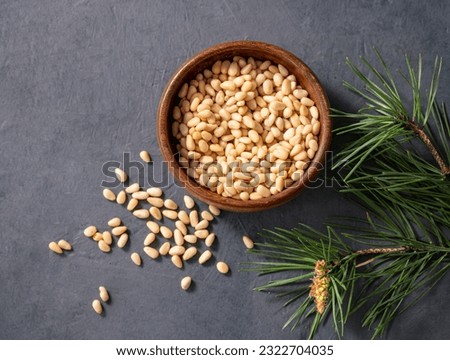 Pine nuts in a bowl and a scattered on a dark background with branches of pine needles. The concept of a natural, organic and healthy superfood and snack. Top 
view and copy space. Royalty-Free Stock Photo #2322704035
