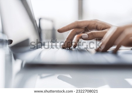 Office environment softly blurred behind, the image focuses on a woman's hands typing on a chic laptop keyboard