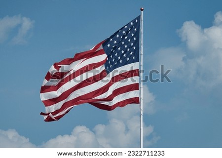 Closeup picture of the American Flag with white fluffy clouds against a blue sky