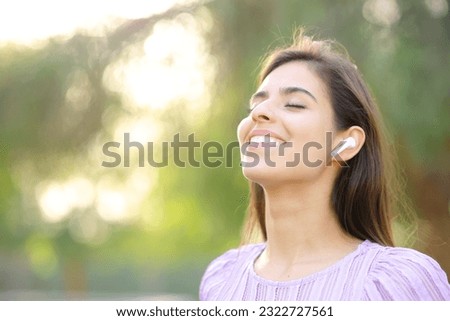 Happy woman breathing fresh air wearing earbud in a green park