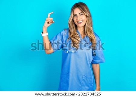 young beautiful doctor woman standing over blue studio background pointing up with fingers number nine in Chinese sign language Jiu