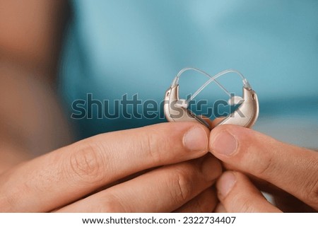 Hearing aids in hands making heart shape over blue background. Closeup of listening device for people with hearing disorder, disfunction. Technology that gives better sense of sound, speach Royalty-Free Stock Photo #2322734407