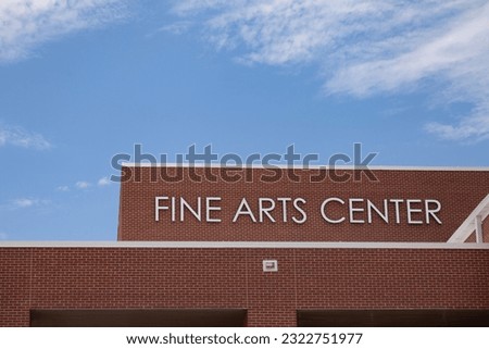 Daytime closeup of a modern brick building with the words Fine Arts Center seen with a blue sky in the background.