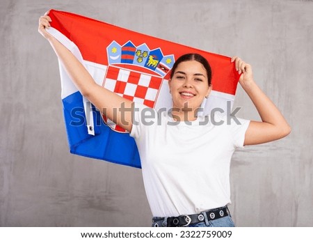 Joyous young woman with Croatia flag in hands posing happily against light unicoloured background