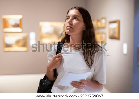 Portrait of a young girl visitor with a paper guide at the exhibition of paintings in the museum Royalty-Free Stock Photo #2322759067