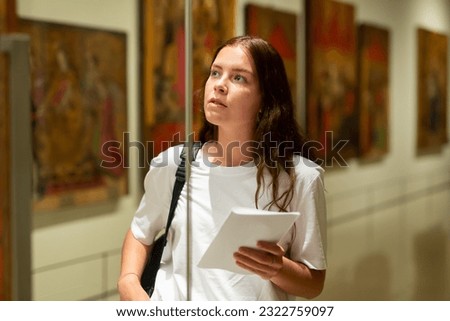 Focused girl visiting an exhibition in a museum looks with interest at the exhibit located behind the glass Royalty-Free Stock Photo #2322759097