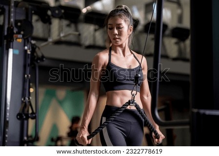 Portrait of a young Asian woman, good looking, shapely, in a black dress. She's working exercise fitness out in a world-class gym.