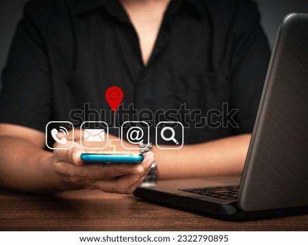 Contact us. Businessman holding a smartphone with a location red pin symbol, search, email, telephone, and address icons while sitting at the table. Customer service call center.