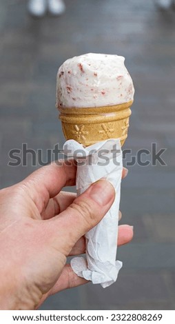 Close up image of girl hand holding fresh waffle cone with vanilla and raspberry ice cream on the wooden background. Walking. Outdoors. High quality photo