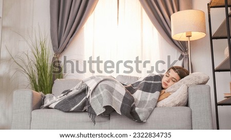 Home relaxation. Sofa rest. Day nap. Satisfied girl sleeping under blanket on comfortable couch enjoying rest on weekend daydream in light room interior. Royalty-Free Stock Photo #2322834735