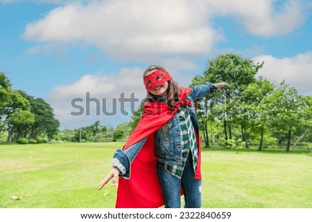 pretty and cute eight-year-old girl wearing a red mask and veil like a super hero is fun to run around in the park.
