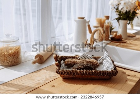 Fresh bread and utensils on the kitchen table, ready to be cooked. Simple modern scandinavian style kitchen, kitchen details, wooden table, bouquet of flowers in a vase on the table. Royalty-Free Stock Photo #2322846957