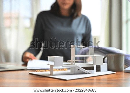 Models of the modern box glass house or energy-saving basic house with blur background of undergraduate architecture students while learning detailed blueprint paper drawing. Focusing on home model.