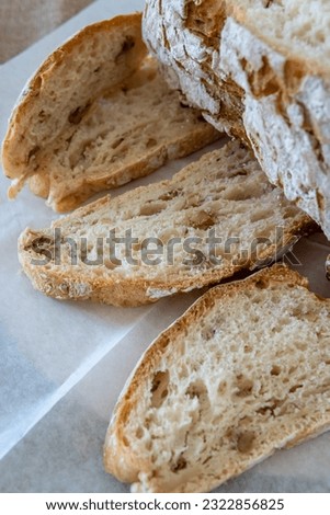 Close up on slices of homemade walnut bread, traditional sourdough bread loaf cut into slices on baking paper. Sliced bread with golden bread crust. Healthy baking concept, top view.