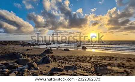 Scenic view during sunset on the volcanic sand beach Playa del Ingles in Valle Gran Rey, La Gomera, Canary Islands, Spain, Europe. Sun beam reflection on water surface. Stones in the foreground Royalty-Free Stock Photo #2322862573