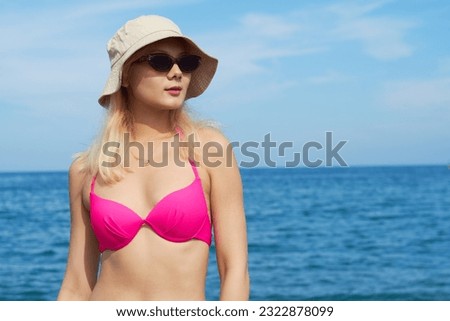 Portrait of girl in a bikini with sunglasses and a hat on the beach looking to the side. Vacation. Summer.