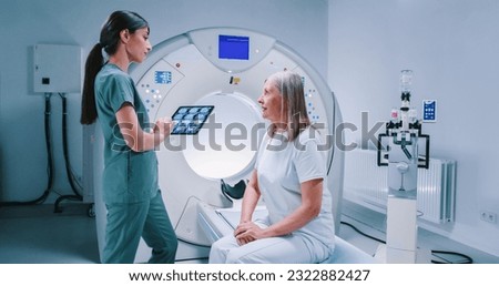 Male doctor and female patient are having discussion at modern tomography laboratory. African American doctor is holding folder and gesturing. Woman sits at MRI bed and talk to doctor. Royalty-Free Stock Photo #2322882427