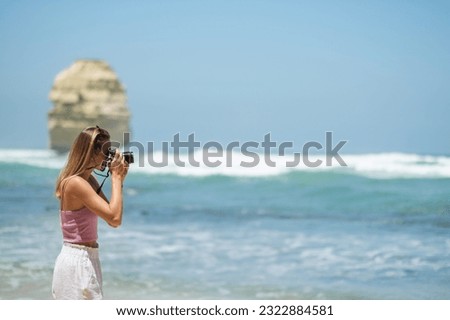 Young beautiful woman walking on the beach and taking photos at Twelve Apostles rock formations at the great ocean road in sunny weather with a blue sky, Victoria, Australia 