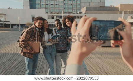 Young cheerful people make a joint photo. Group of students smiling while looking at mobile phone camera while standing outside
