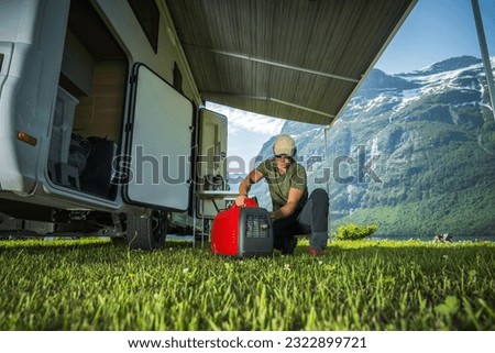 Caucasian Tourist and RV Owner Running Red Portable Inverter Generator To Hook Up the Camper Van. Vacation On the Road Theme. Royalty-Free Stock Photo #2322899721