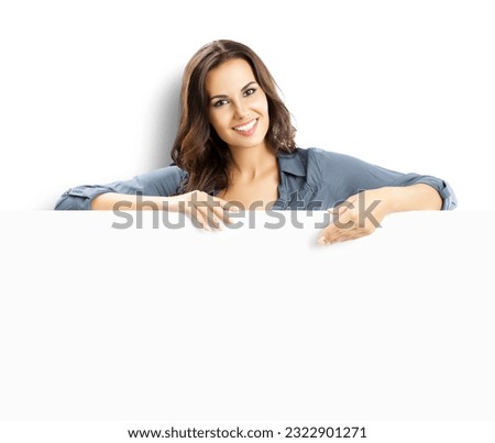 Happy smiling brunette young woman standing behind, peeping from blank banner or showing mock up signboard with copy space for some text, isolated over white background.