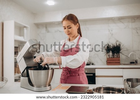 Woman wearing apron baking cookies in a cozy kitchen. The housewife makes the dough for the cake in the planetary mixer. Homemade cakes or pies. Royalty-Free Stock Photo #2322905181