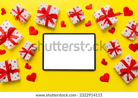 Top view of digital tablet with gift boxes and hearts on colorful background. Tablet with black screen with Holiday decorations gift box top view.