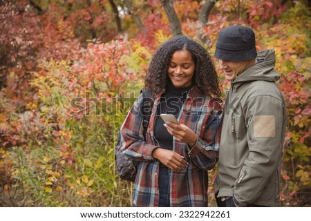 Young beautiful couple looking on photos on phone isolated over colorful autumn landscape. Couple doing hiking on warm fall day . Concept of leisure time, weekends, activity, sport. Copy space for ad