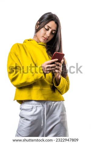 Portrait studio picture of beautiful caucasian model woman posing in yellow hoodie, sending sms with smartphone with white bright background