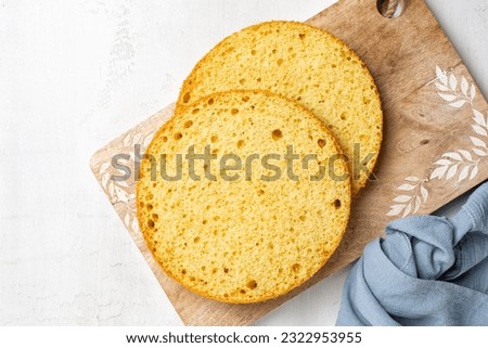 Cooking and baking round vanilla sponge cake or chiffon cake, two cut layers with texture. Homemade culinary, dessert. Top view, white background.  Royalty-Free Stock Photo #2322953955