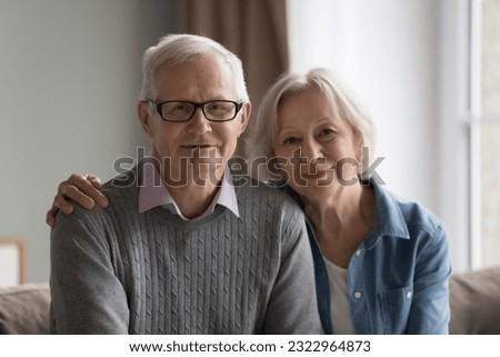Senior wife and husband, baby boomer generation couple smile look at camera rest on couch in living room. Profile picture of videocall participants. Calm wellbeing retired life, happy strong marriage