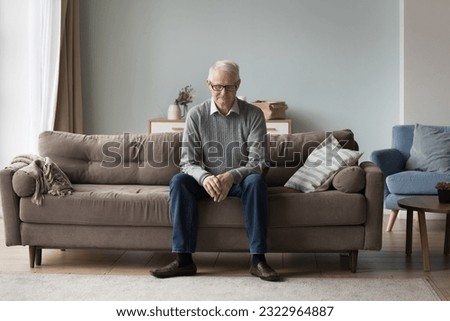 Upset thoughtful retired single man sit on couch alone, feels abandoned, suffer from weakness, having ageing disorders, grieving about past, missing for grown up children, looks deep in sad thoughts Royalty-Free Stock Photo #2322964887