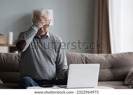 Confused retired man feeling unhappy suffer from lack of money, sitting in living room use laptop calculate monthly budget, pay for service online, has financial difficulties. Overspend, debt, crisis Royalty-Free Stock Photo #2322964973