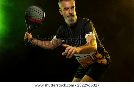 Padel tennis player with racket. Man athlete with paddle tenis racket on court with neon colors. Sport concept. Download a high quality photo for the design of a sports app or betting site.