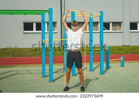Focused teenager working on his body using resistance rubber performs strength training. Preparing for the season. Exercising with your own body. Outdoor workout playground. Upper body.