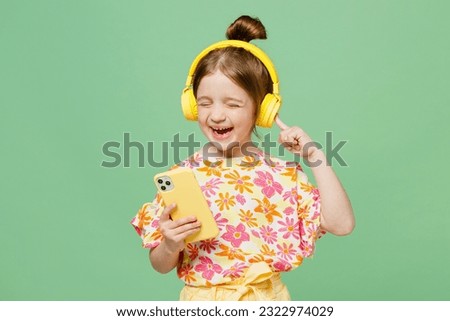 Little fun child kid girl 6-7 years old wear casual clothes headphones listen music use mobile cell phone isolated on plain pastel green background studio. Mother's Day love family lifestyle concept