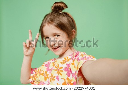 Close up happy little child kid girl 6-7 years old wear casual clothes have fun do selfie shot pov on mobile cell phone show v-sign isolated on plain green background. Mother's Day love family concept Royalty-Free Stock Photo #2322974031