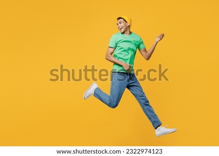 Full body profile young man of African American ethnicity he wears casual clothes green t-shirt hat jump high look aside pov play guitar isolated on plain yellow background studio. Lifestyle concept Royalty-Free Stock Photo #2322974123