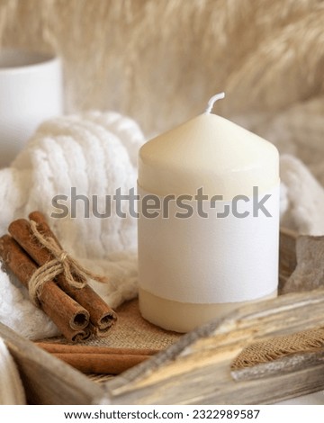 Candle with blank paper label on wooden tray near cinnamon, dried pampas grass and natural decor, Close up, copy space. Boho packaging mock up. Winter Christmas home 
