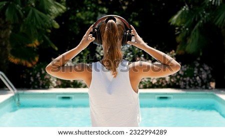 Slow Motion Of Young Woman Putting On Headphones, Beautiful Garden and Swimming Pool in the Background
