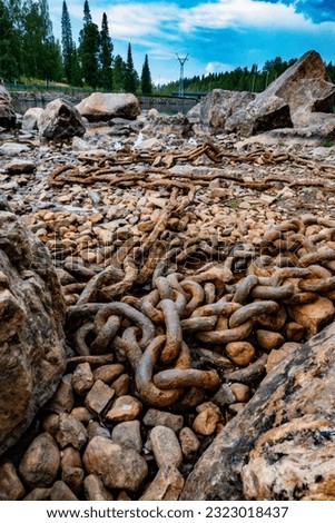 Old and rusty chain. Beautiful summer day in a river landscape. Bunch of rocks.