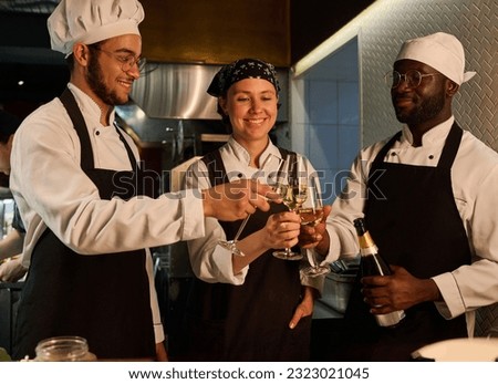 Three happy young intercultural cooks celebrating life event with champagne Royalty-Free Stock Photo #2323021045
