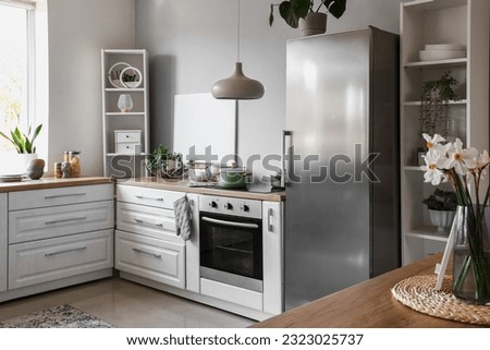 Interior of light kitchen with stylish fridge, counters and shelving units