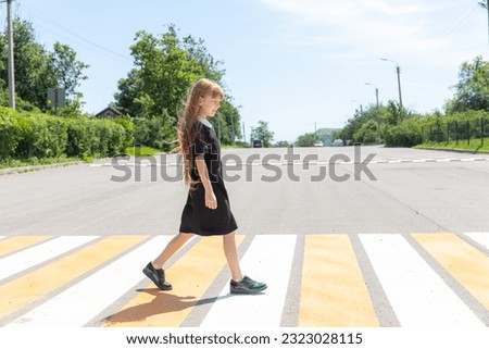 Schoolgirl crossing road on way to school. Zebra traffic walk way in the city. Concept pedestrians passing a crosswalk. Stylish little girl walking with backpack. Active child.