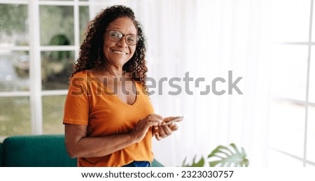 Senior woman living alone uses her smartphone to stay connected and feel secure, with the ability to make calls, send texts, and access the friendly online communities of fellow senior citizens. Royalty-Free Stock Photo #2323030757