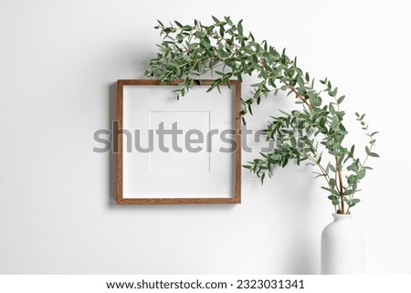 Blank square frame mockup for artwork or print on white wall with eucalyptus plant in vase, frame with copy space