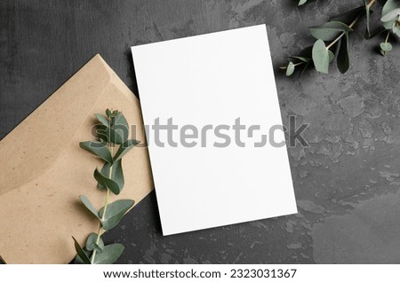 Invitation or greeting card mockup with fresh eucalyptus twigs and envelope on dark stony background